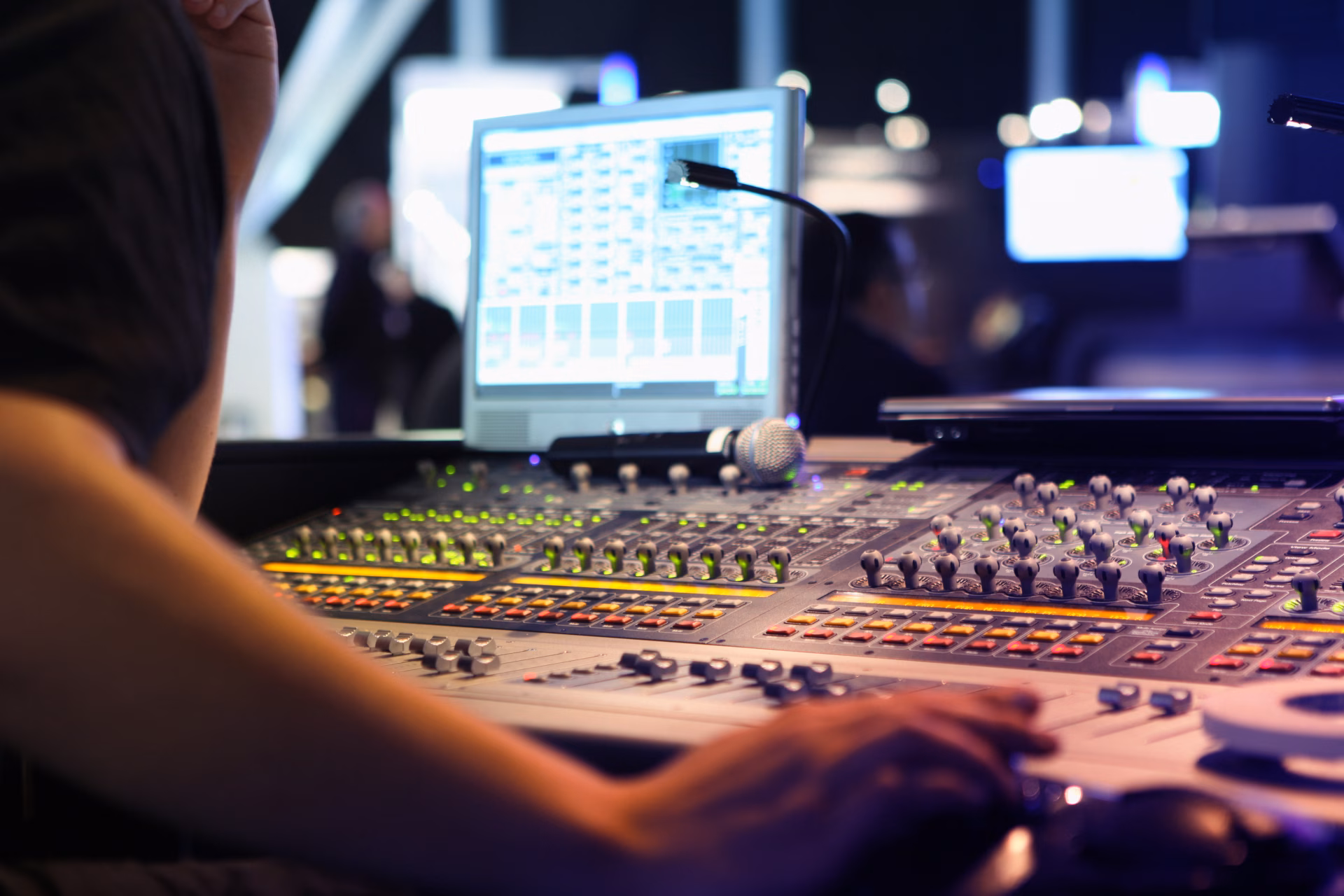 Engineer's hands operating a mixing console in front of a monitor
