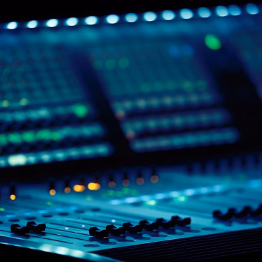 Close-up of a digital mixing console with backlit faders and channel strips