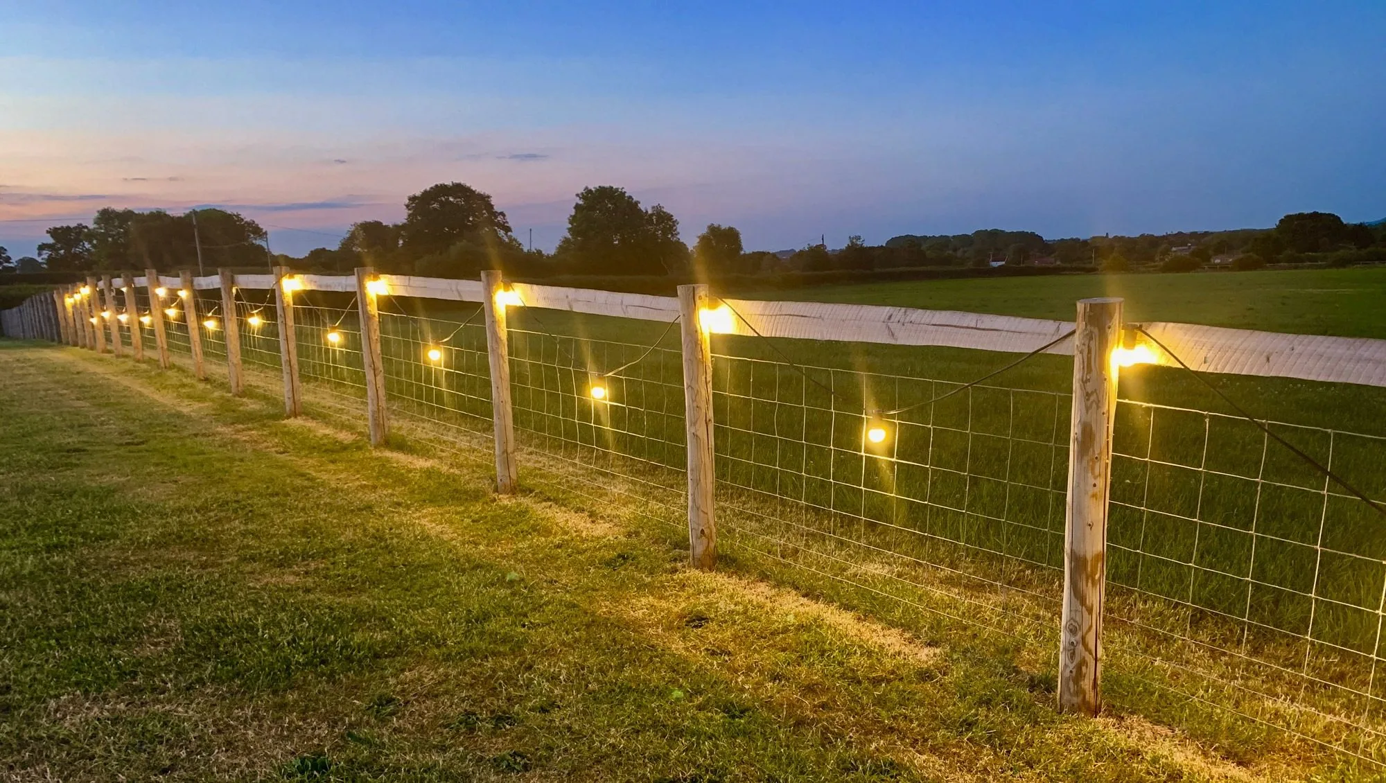 A wooden fence on a summers evening with festoon lighting hung
