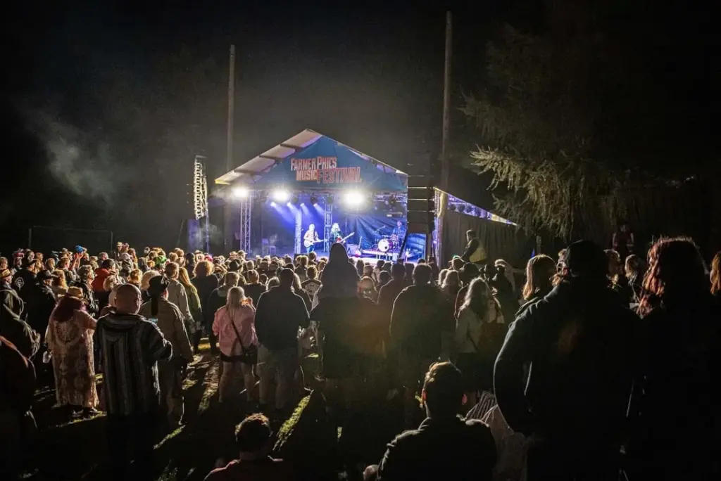 Floodlit tent stage in a field at night with a crowd in front