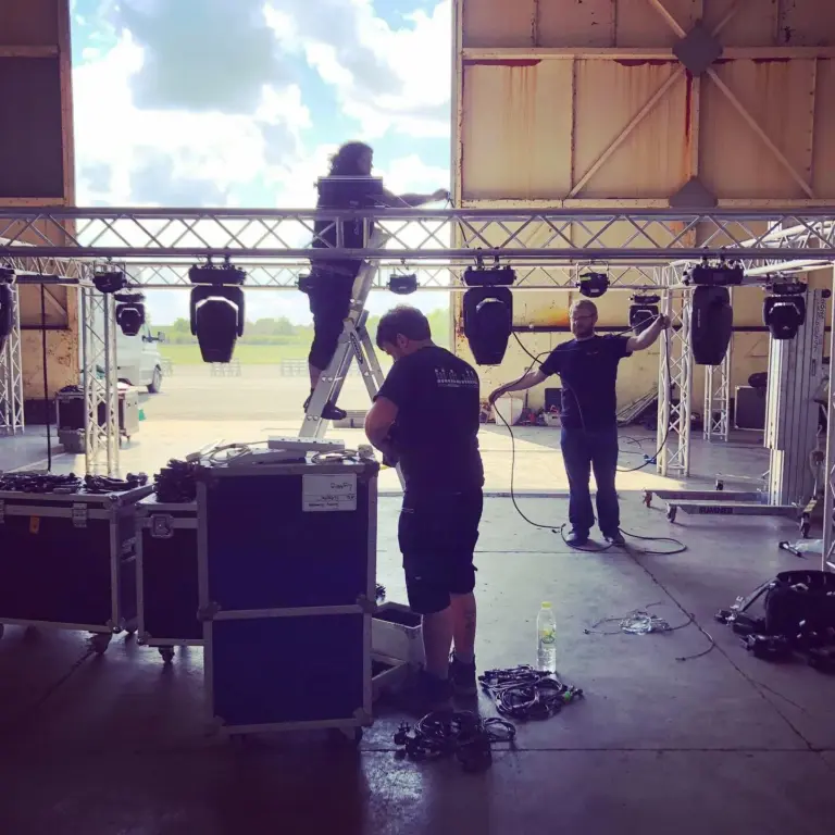 Two crew members rigging moving head lights on a truss, with flight cases in the foreground