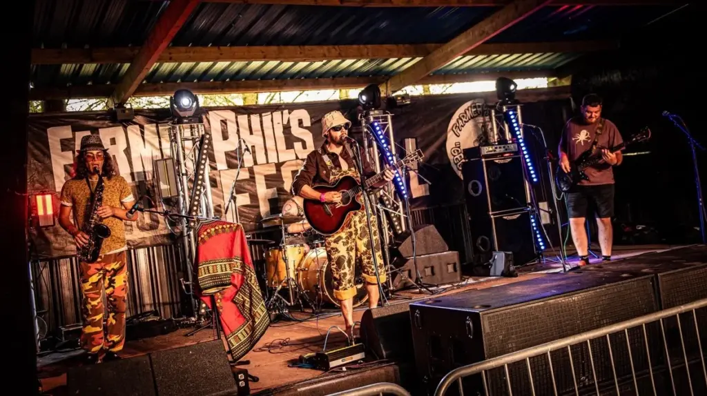 Band performing on a small stage hung with festoon lights, with crowd barriers in front
