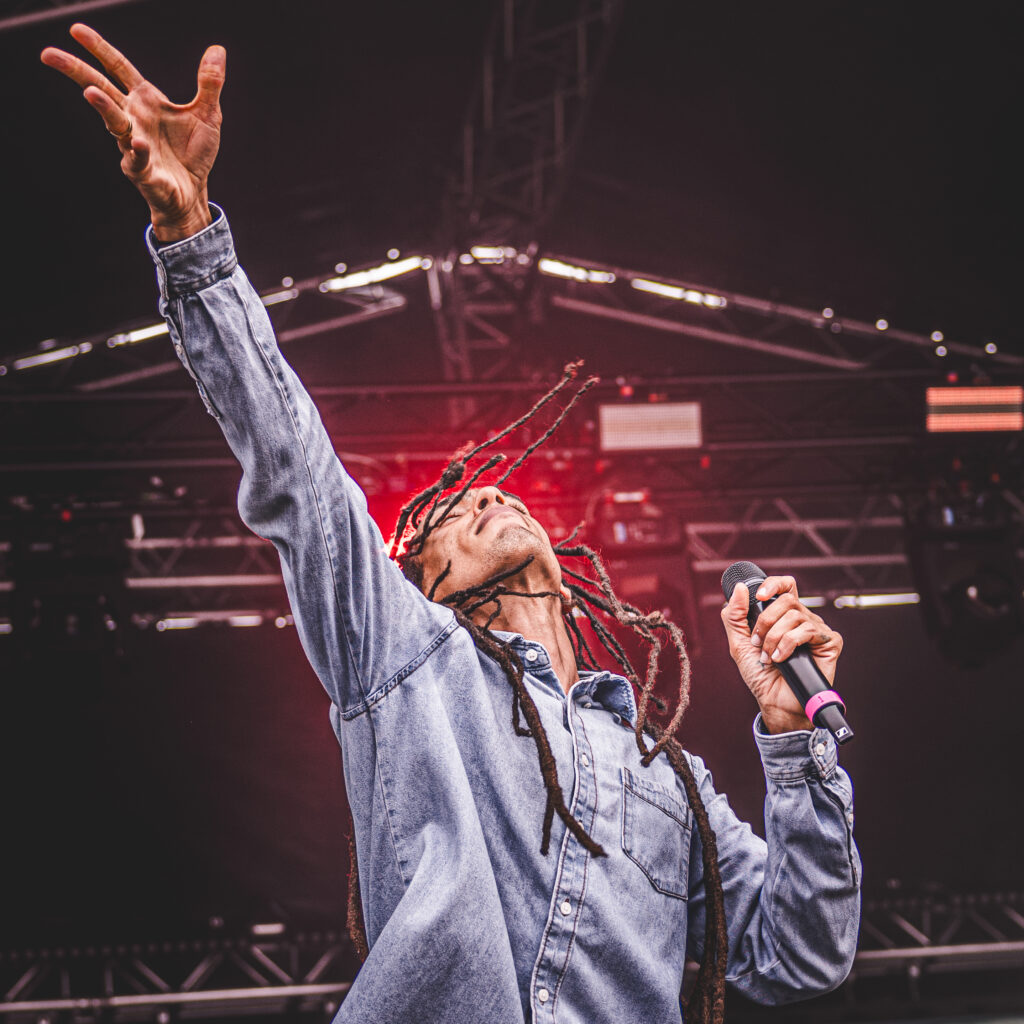 Performer on stage with arms raised under the lighting truss