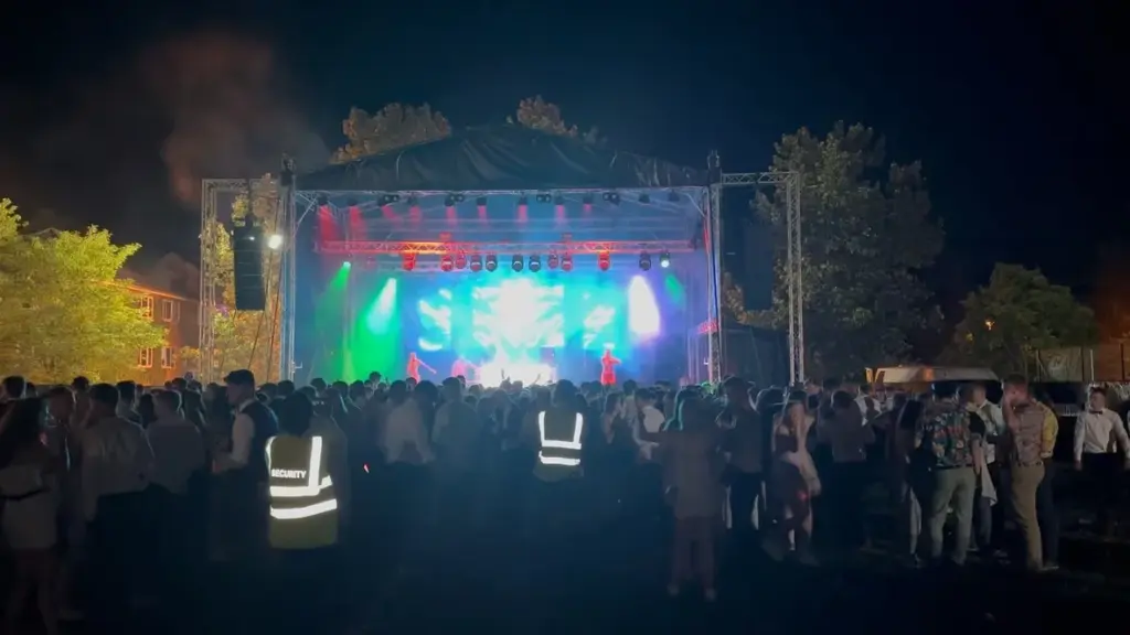 Outdoor stage lit in green and blue at night with a crowd gathered in front