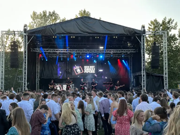 Crowd in front of an outdoor festival stage with a lit truss rig and video screens