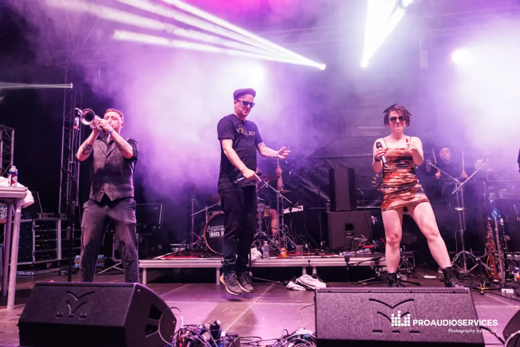 Brass section playing on stage under purple and pink lighting with haze