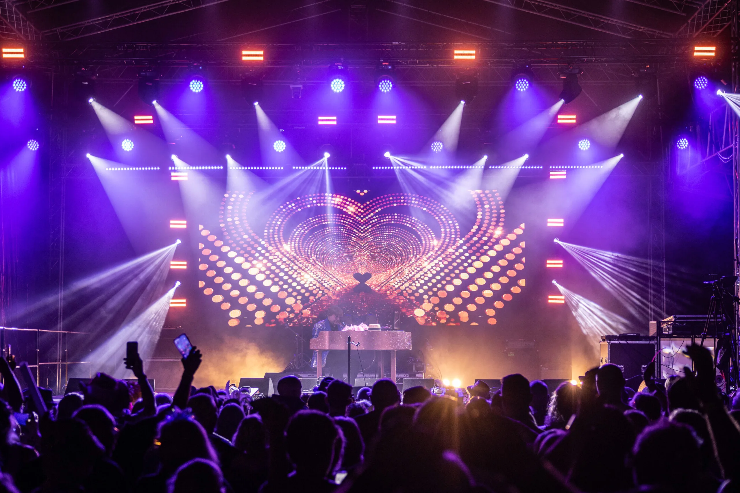 A crowd of people silhouetted by lights shining out from a stage