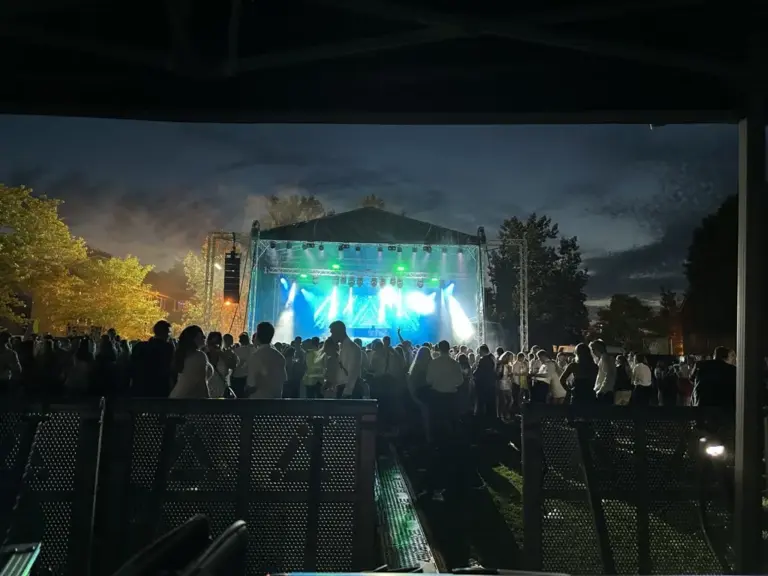 Large stage outside at night with video wall at the back and lights shinning out over the adience in front.