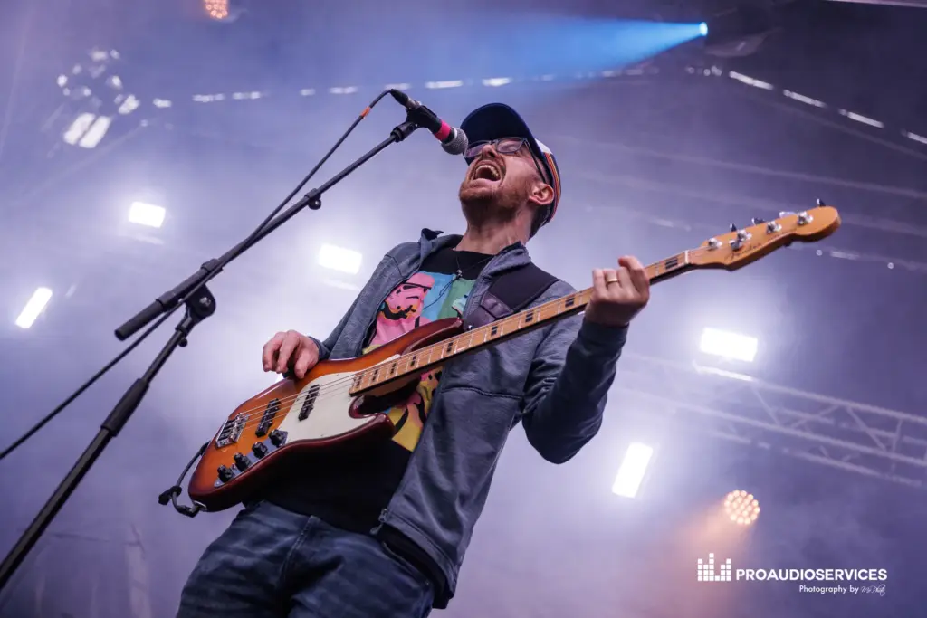 Guitarist singing into a microphone on stage under blue stage lighting
