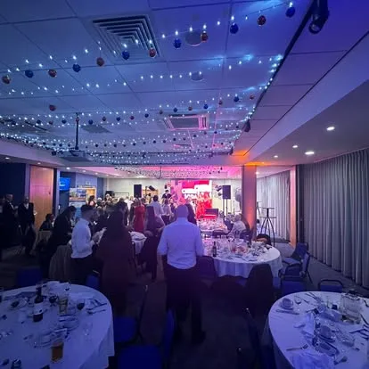 Gala dinner room with round tables, a star-lit ceiling and the stage lighting at the far end