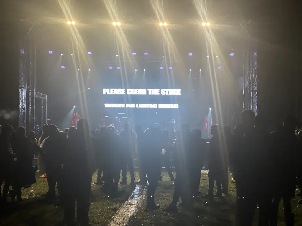 Dark crowd silhouettes in front of a stage with a text screen at Heal Festival