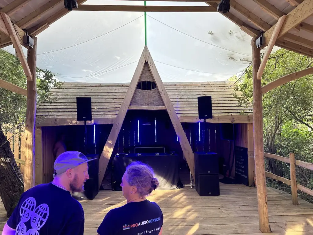 Wooden-roofed pavilion stage with sound equipment and two people in the foreground