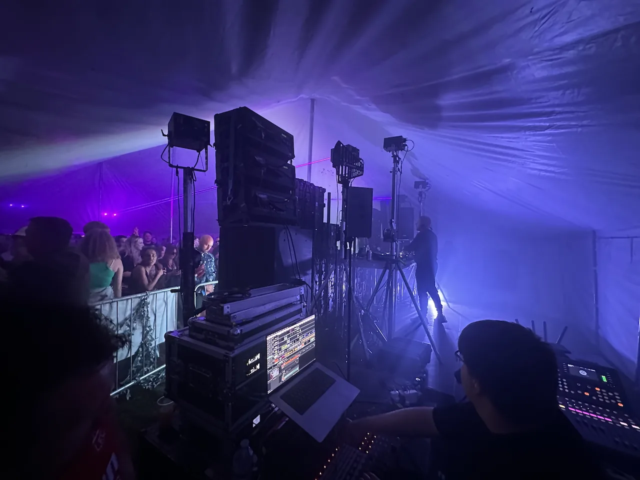 From the back of a stage looking side on. There is a DJ playing and some speakers