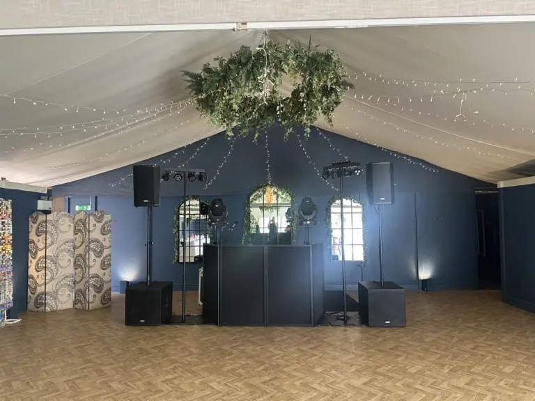 Speakers set up around a DJ table in a room with white drapes hanging from the ceiling, ready for a wedding