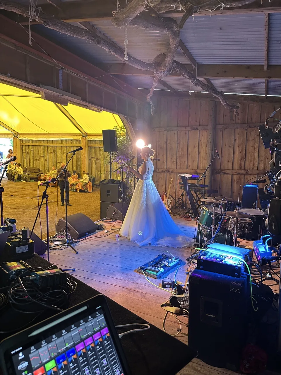 Bride wearing a long white wedding dress stood on a stage talking to her guests.
