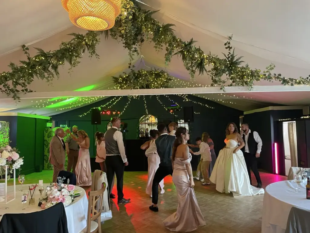 Wedding marquee with a floral garland and a green-lit backdrop as the couple dance