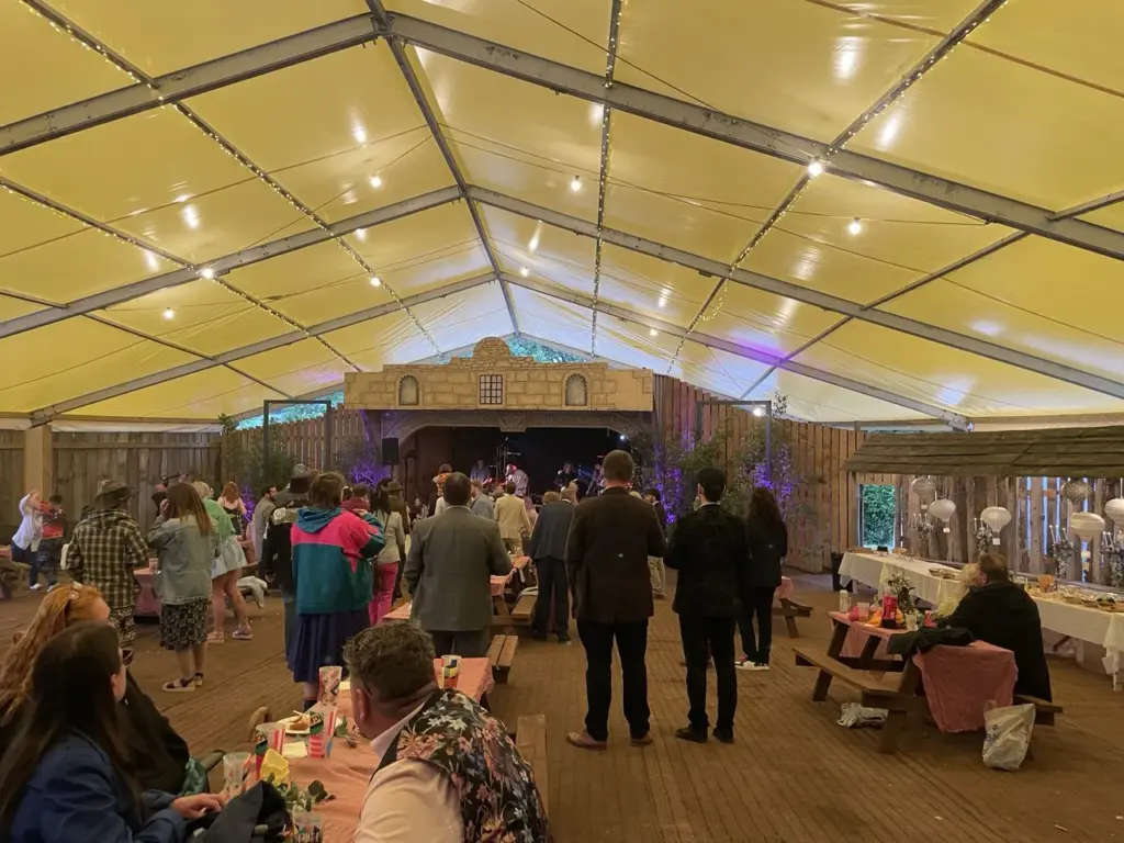 Guests mingling in a marquee with a yellow-lit roof and festoon lighting