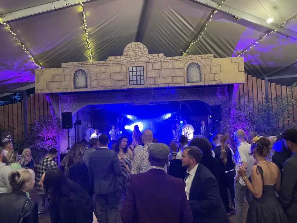 Wedding guests dancing in a marquee lit in blue in front of a decorative backdrop