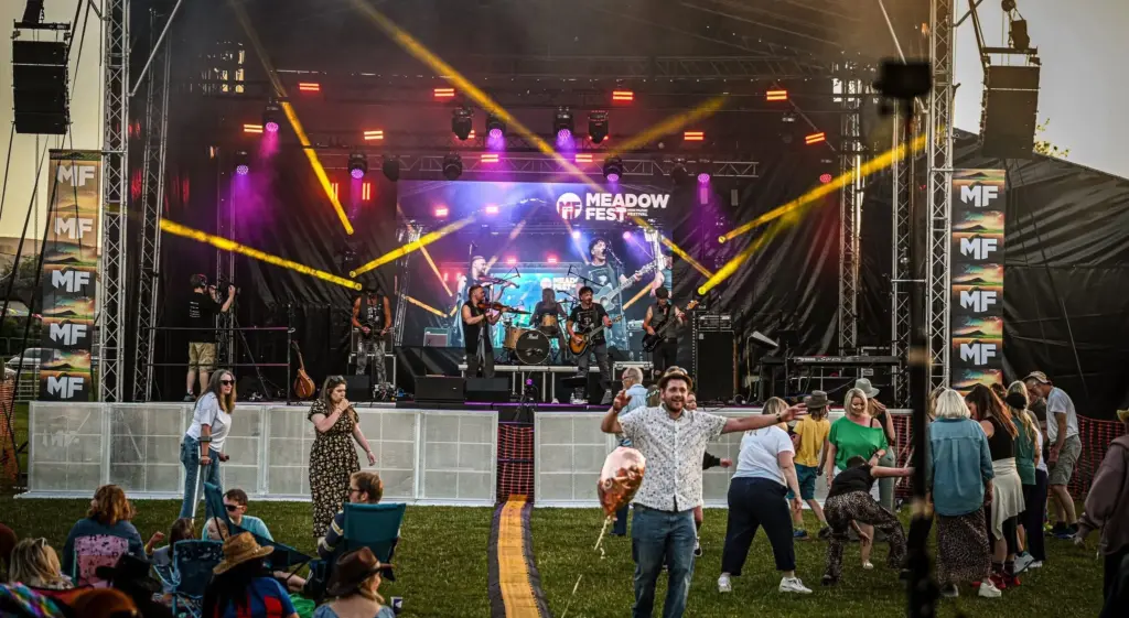 Stage with orange and magenta lighting and a small crowd in front at Meadowfest