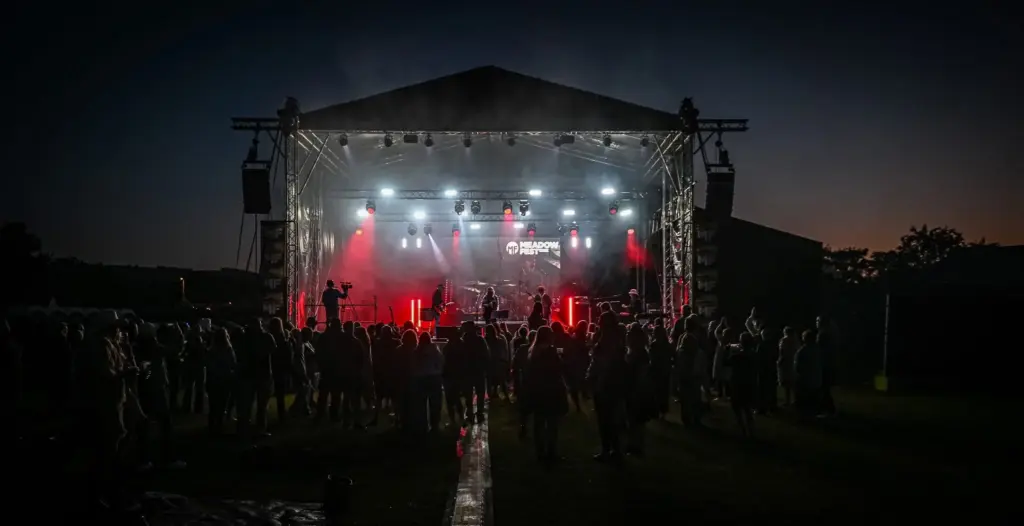 Small stage lit in red and blue in a dark field at dusk at Meadowfest
