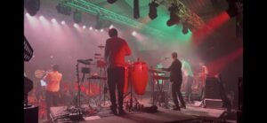 Band playing on stage with red and green lights shinning down on them.