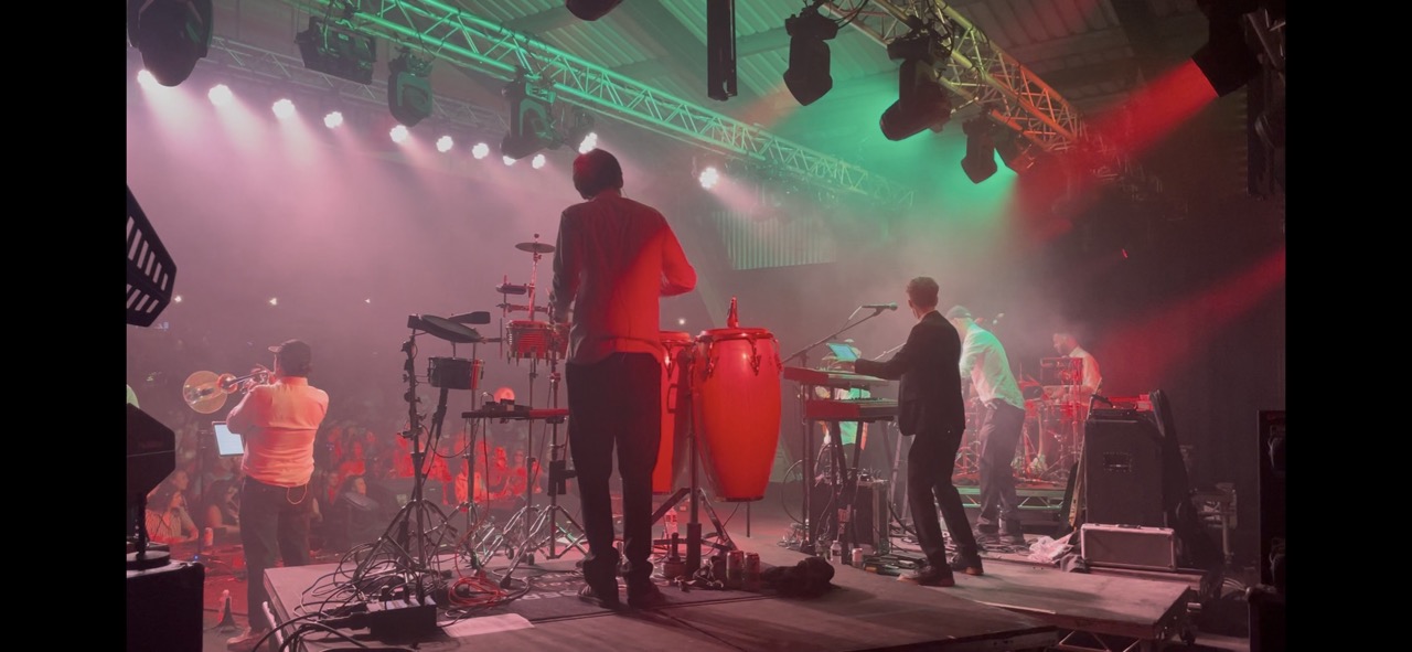 Band playing on stage with red and green lights shinning down on them.