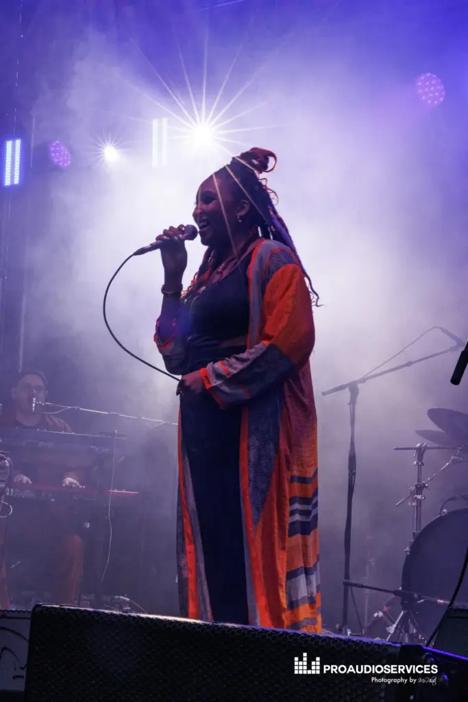 Singer holding a microphone on stage against a blue and purple lit haze