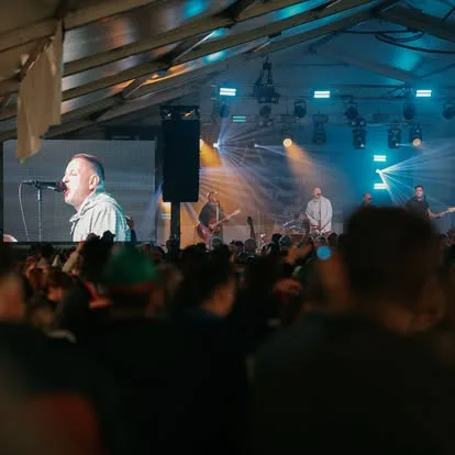 Singer on stage inside the marquee at Oktoberfest with a speaker stack and lighting behind