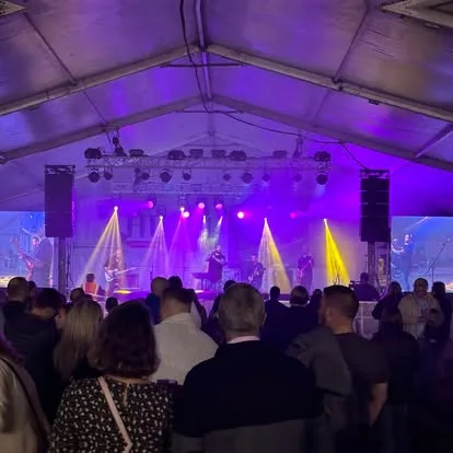 Crowd at the Oktoberfest marquee with purple and yellow stage lighting beams overhead