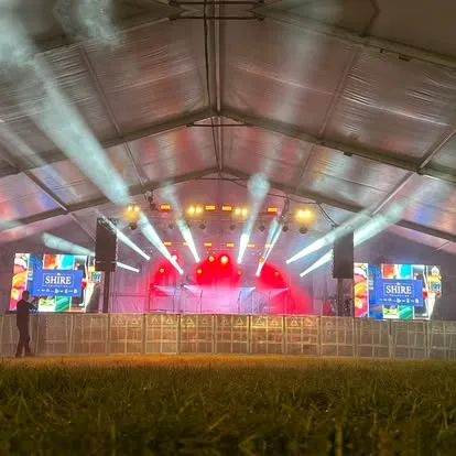 Marquee at dusk with a lighting rig beaming out and LED screens either side of the stage
