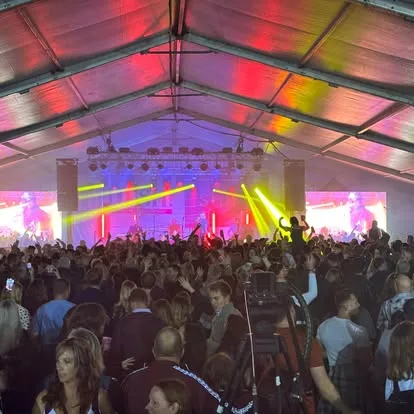 Crowd in front of a stage inside a marquee lit in pink, red and yellow at Oktoberfest