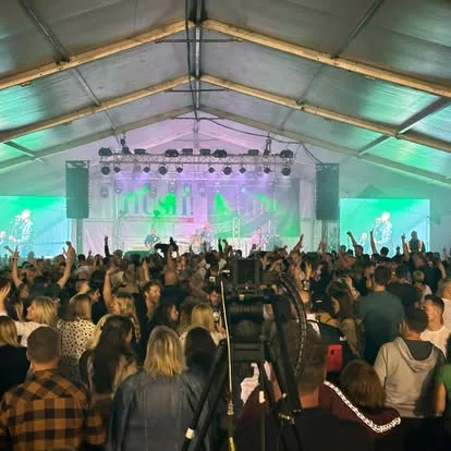 Crowd in a lit marquee at Oktoberfest with green stage lighting and the sound desk in the middle