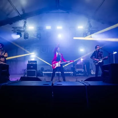 Two guitarists on a blue-lit stage with haze and speaker stacks around them