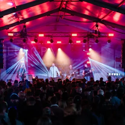 Band on stage under a red and magenta lighting rig with light beams cutting through the haze
