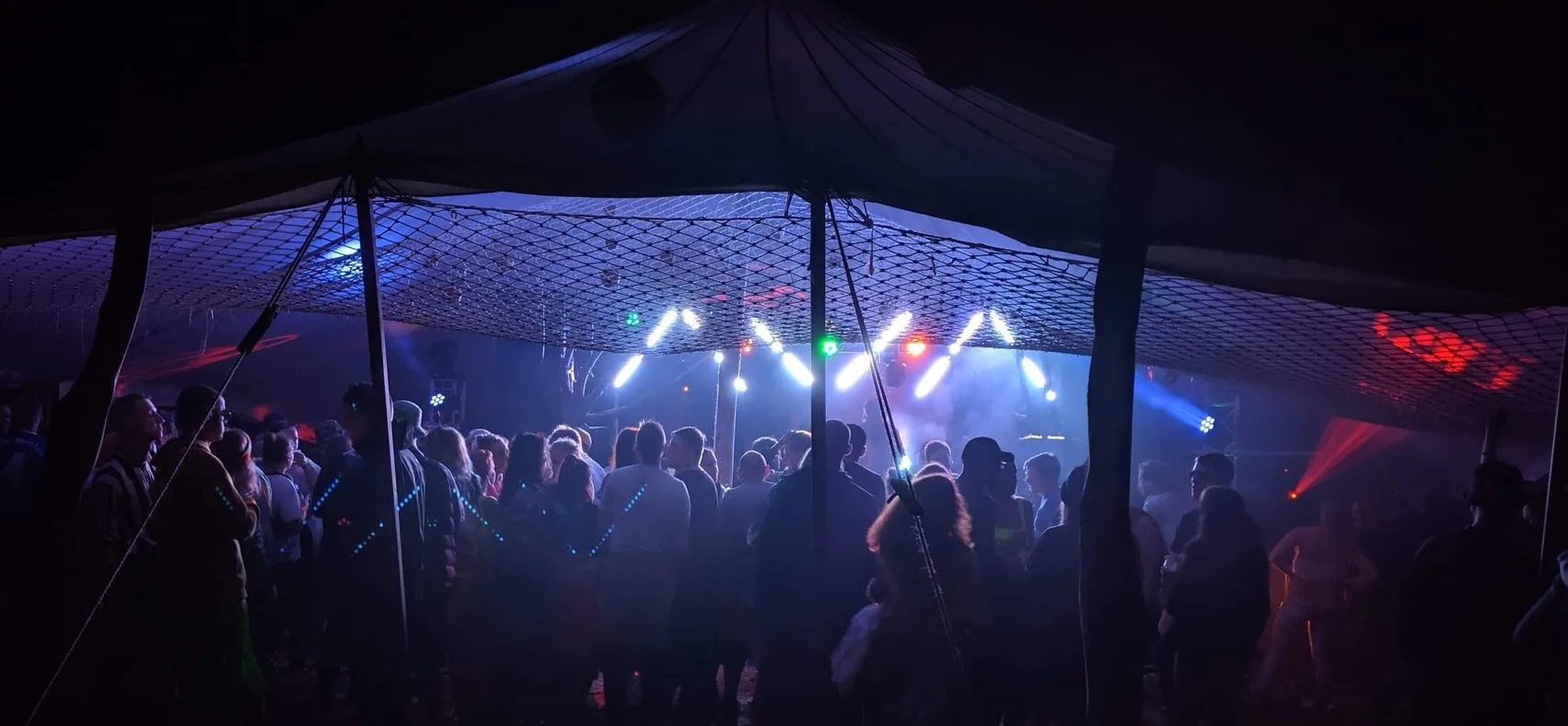People Dancing Under stretch tent at music festival with colorful lighting display