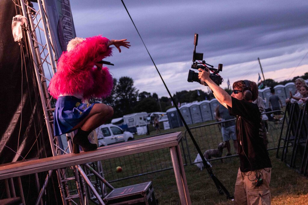Performer in a red top on stage with a camera operator filming alongside