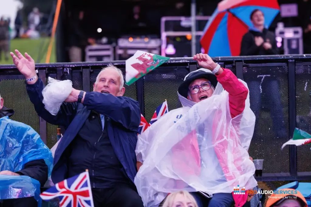 Audience in rain ponchos and waving flags dancing in front of the stage