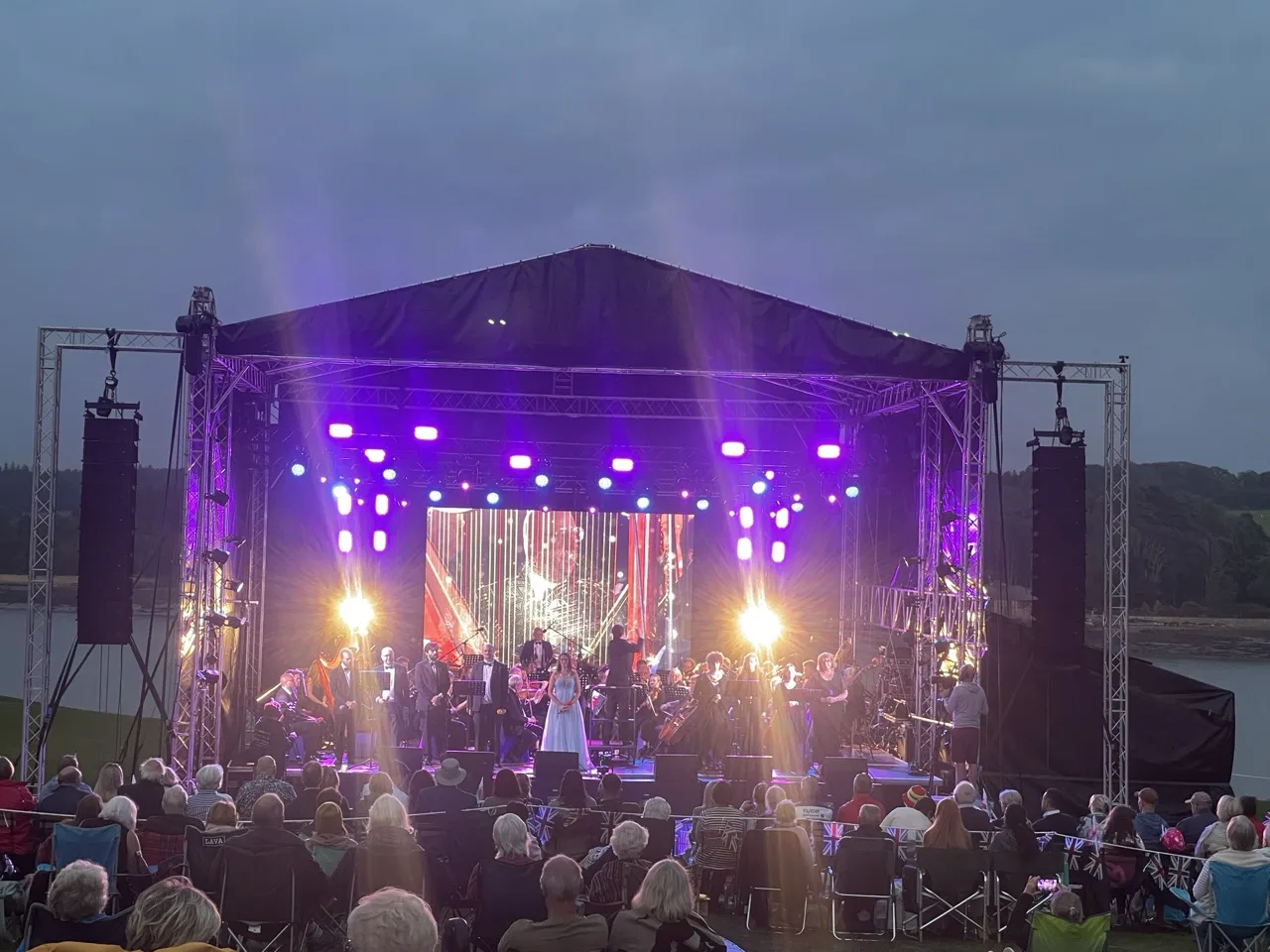 Audience sat down watching an orchestra and a singer ona stage with video wall at the back and lights above.