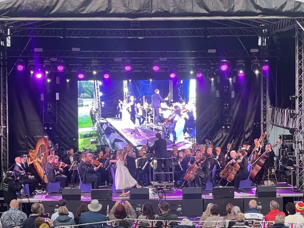 Orchestra on a purple-lit stage with a video screen showing the soloist
