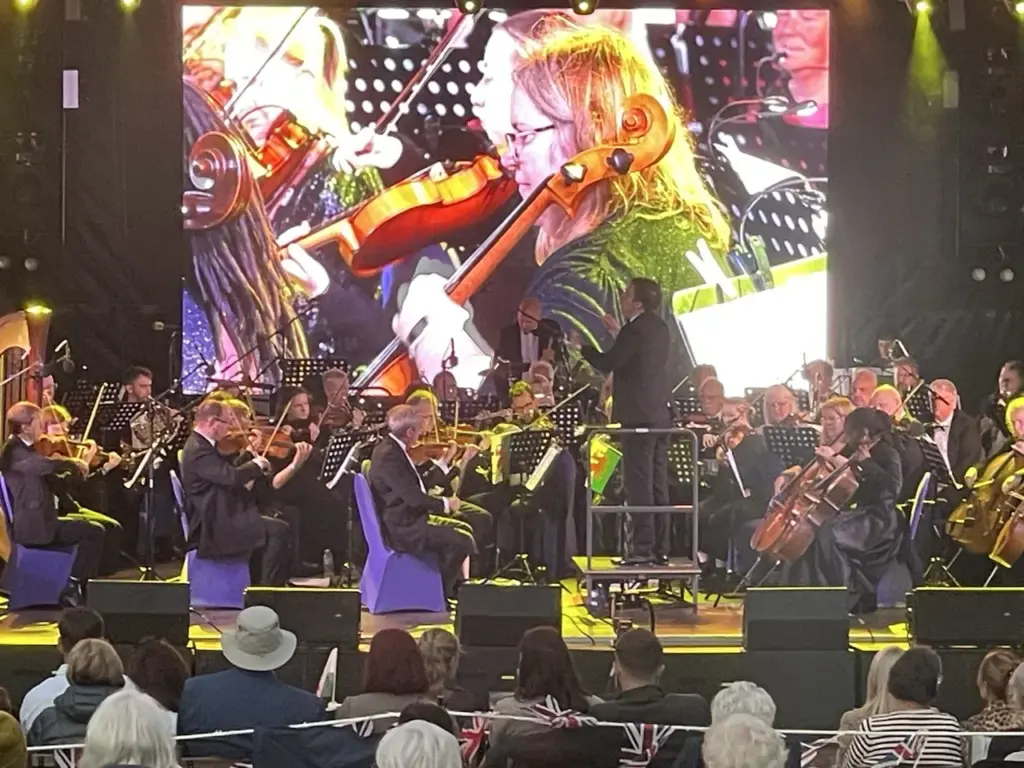 Close view of the orchestra's string section with a violinist shown on the large LED screen behind
