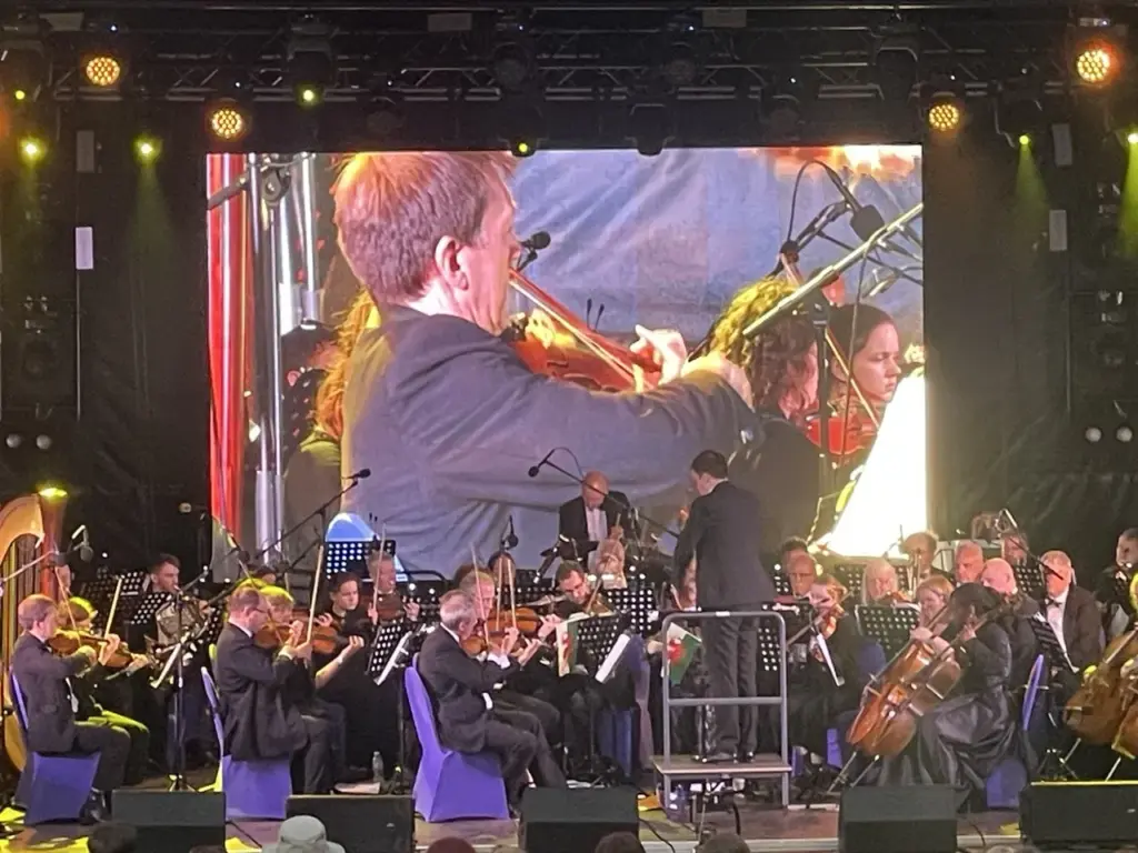 Violinists on stage with a large LED screen showing a close-up of the performer