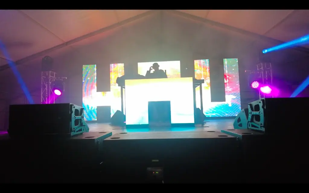 Stage inside a marquee with an LED video wall showing coloured graphics and a lighting rig above