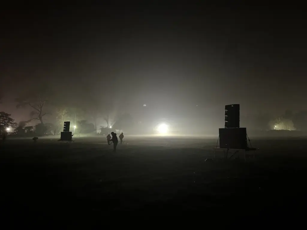 Dark field at night with a glow on the horizon and a speaker tower set up for a firework show