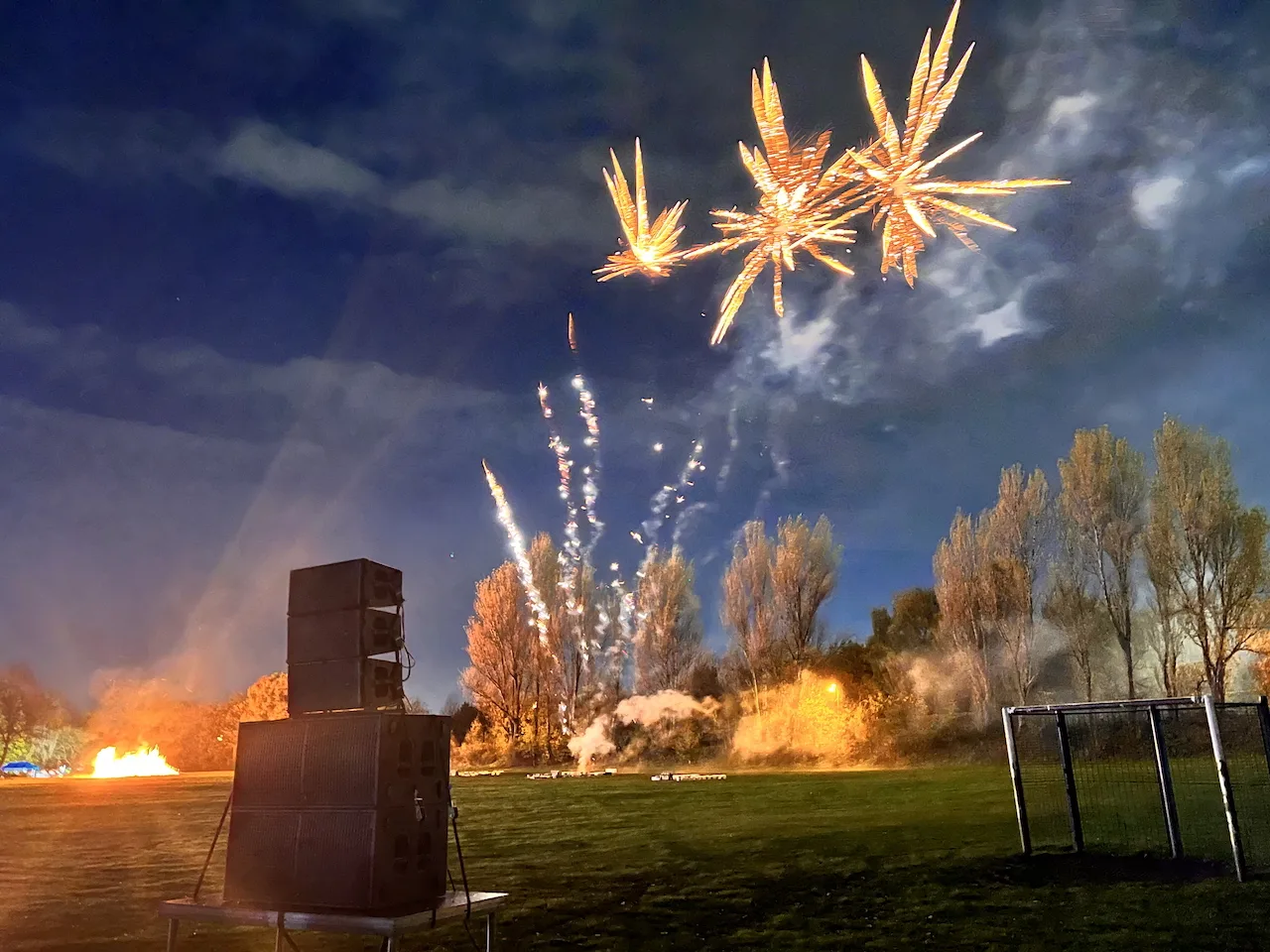 Fireworks exploding in the sky above a set of speakers that are st-up in a field.