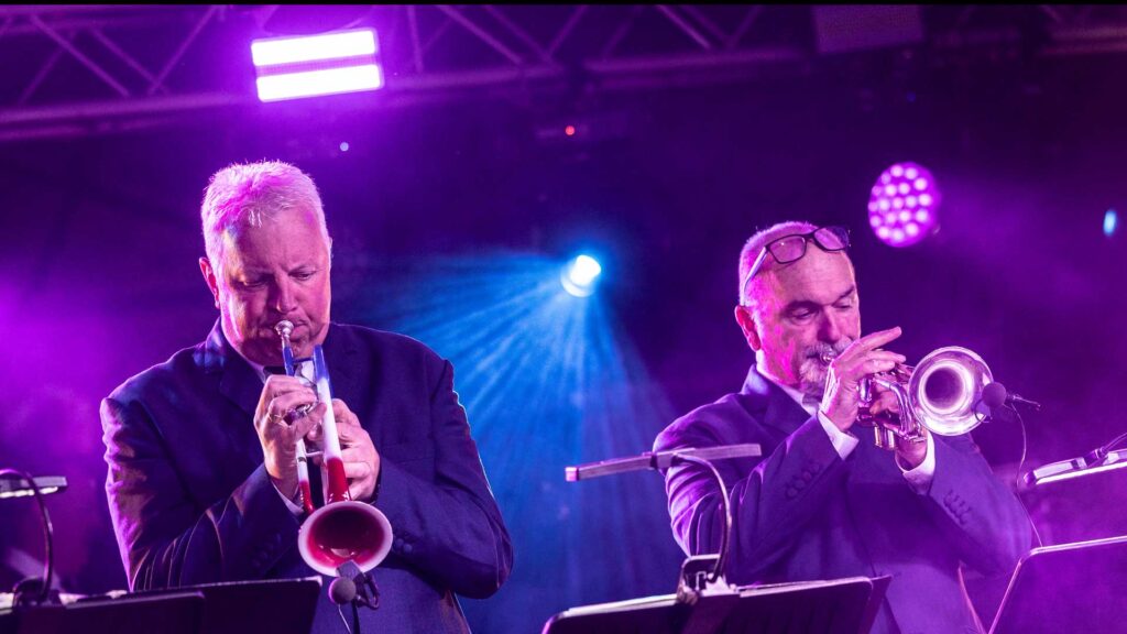 Two brass players performing on stage under purple stage lighting at Farmer Phil's Festival
