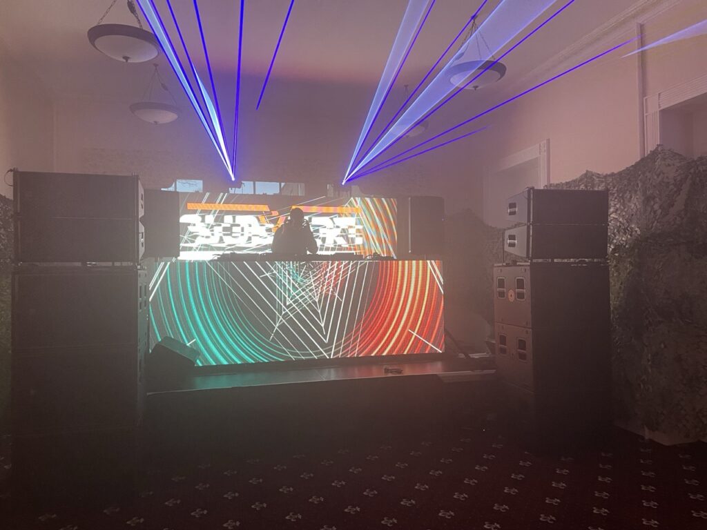 DJ booth with laser beams and a lit LED front at a mansion party