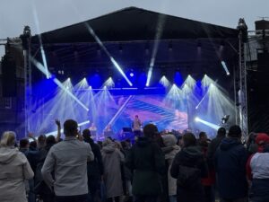 Acrowd of people watching an orchestra play on a stage with lights shinning out on them