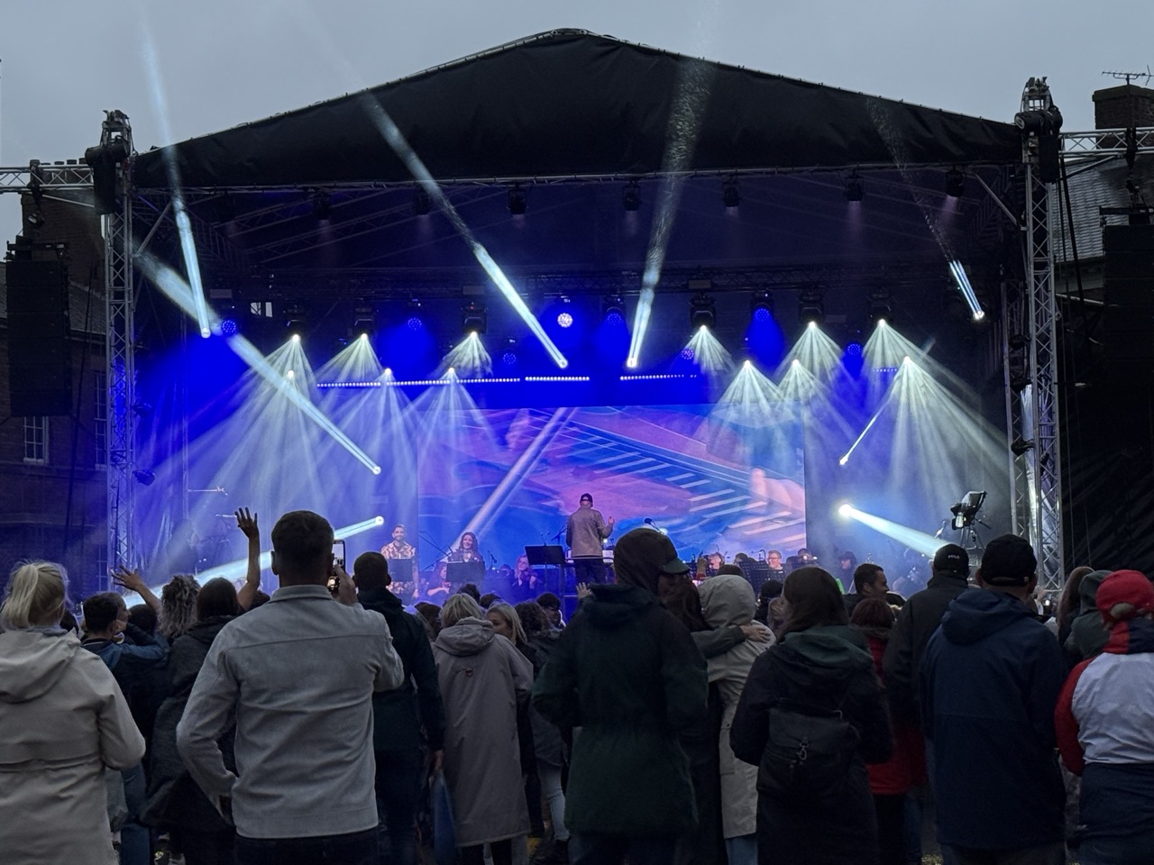 Acrowd of people watching an orchestra play on a stage with lights shinning out on them