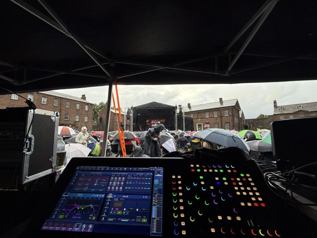 Mixing console under a canopy with brick buildings behind at the Proms in Carlisle