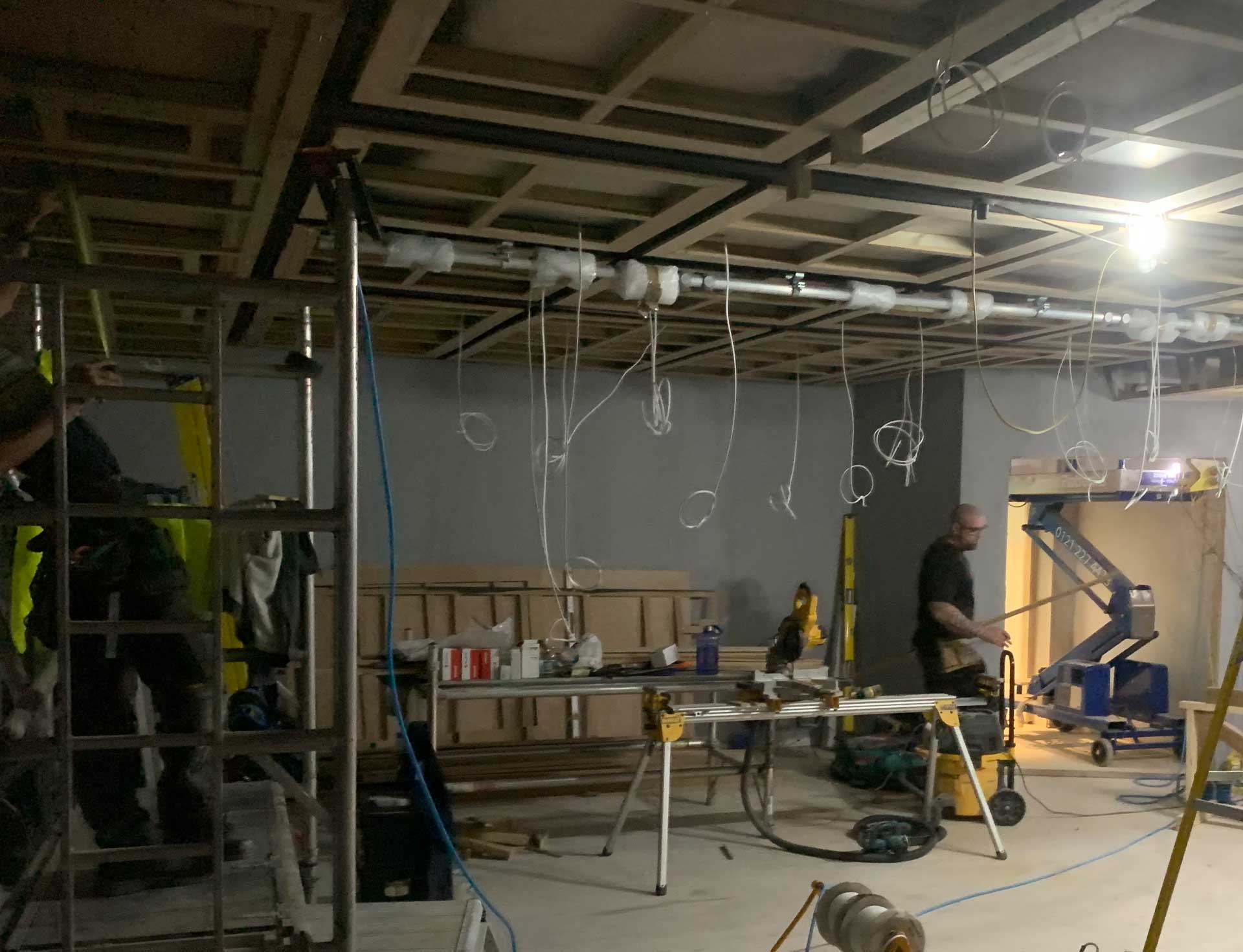 Studio space under construction with cable runs, ceiling framework and installers at work